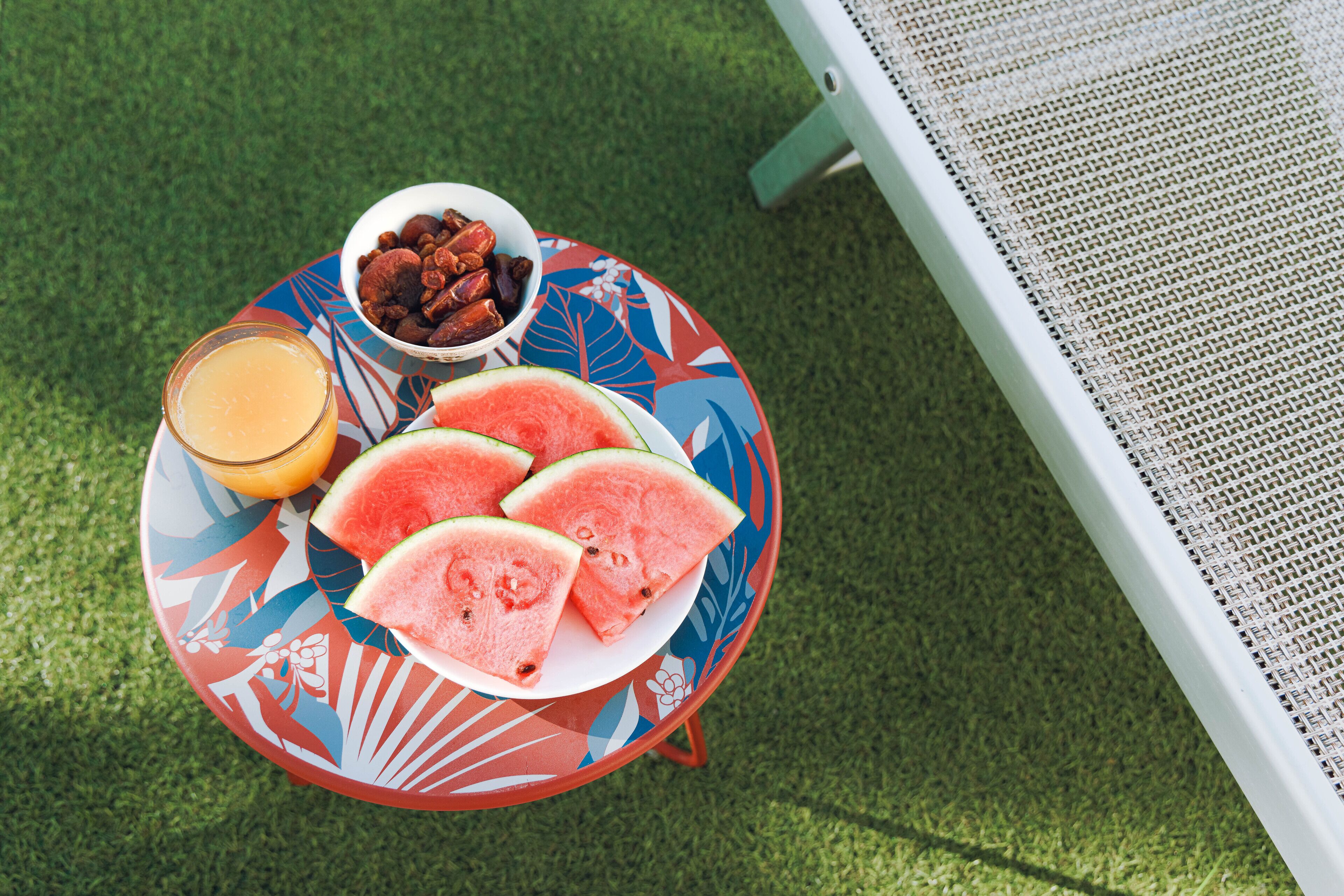 A table with a plate of watermelon slices, a bowl of nuts, and a glass of orange juice.