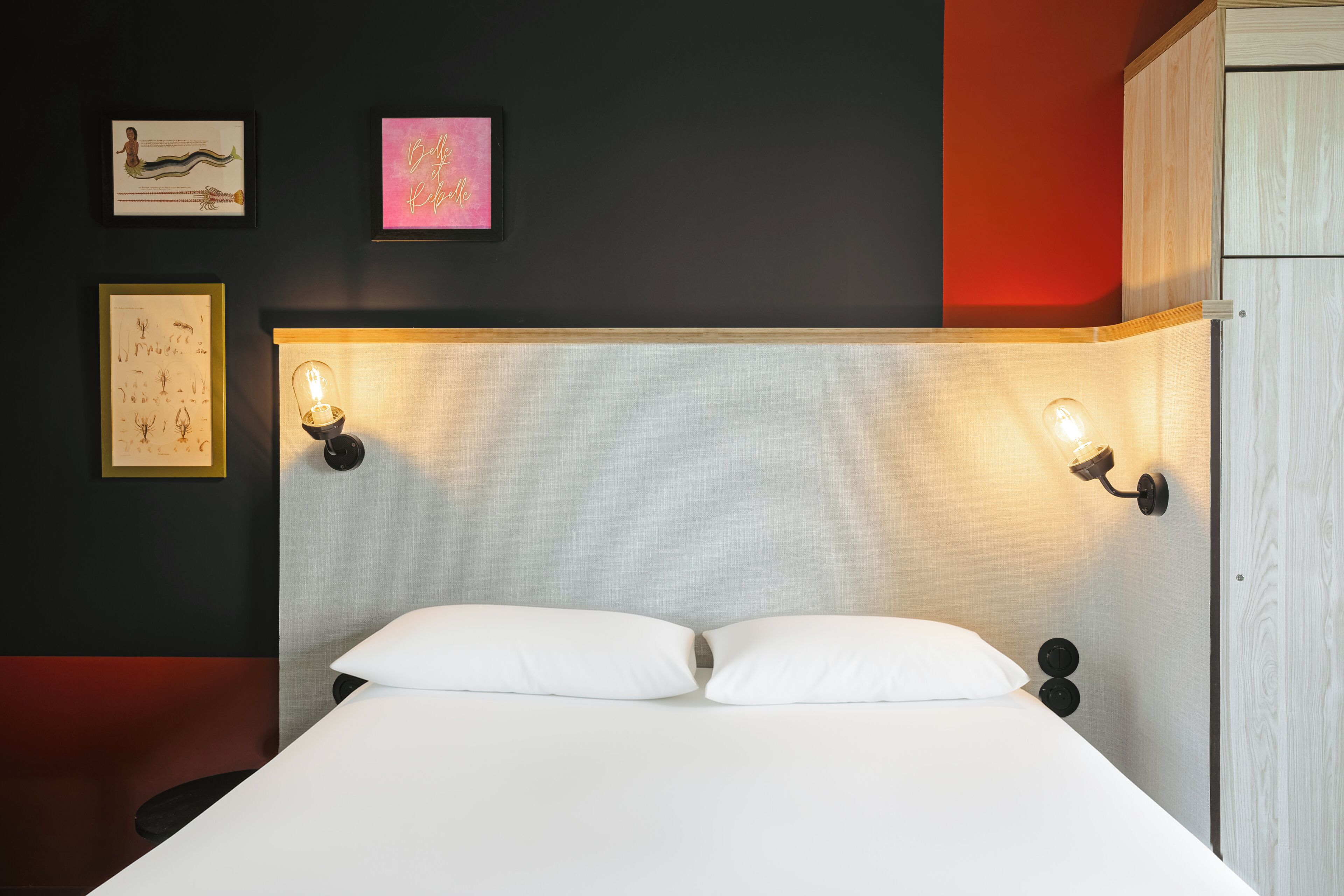 A bed with two white pillows, a headboard with a textured fabric, and two wall-mounted light fixtures.