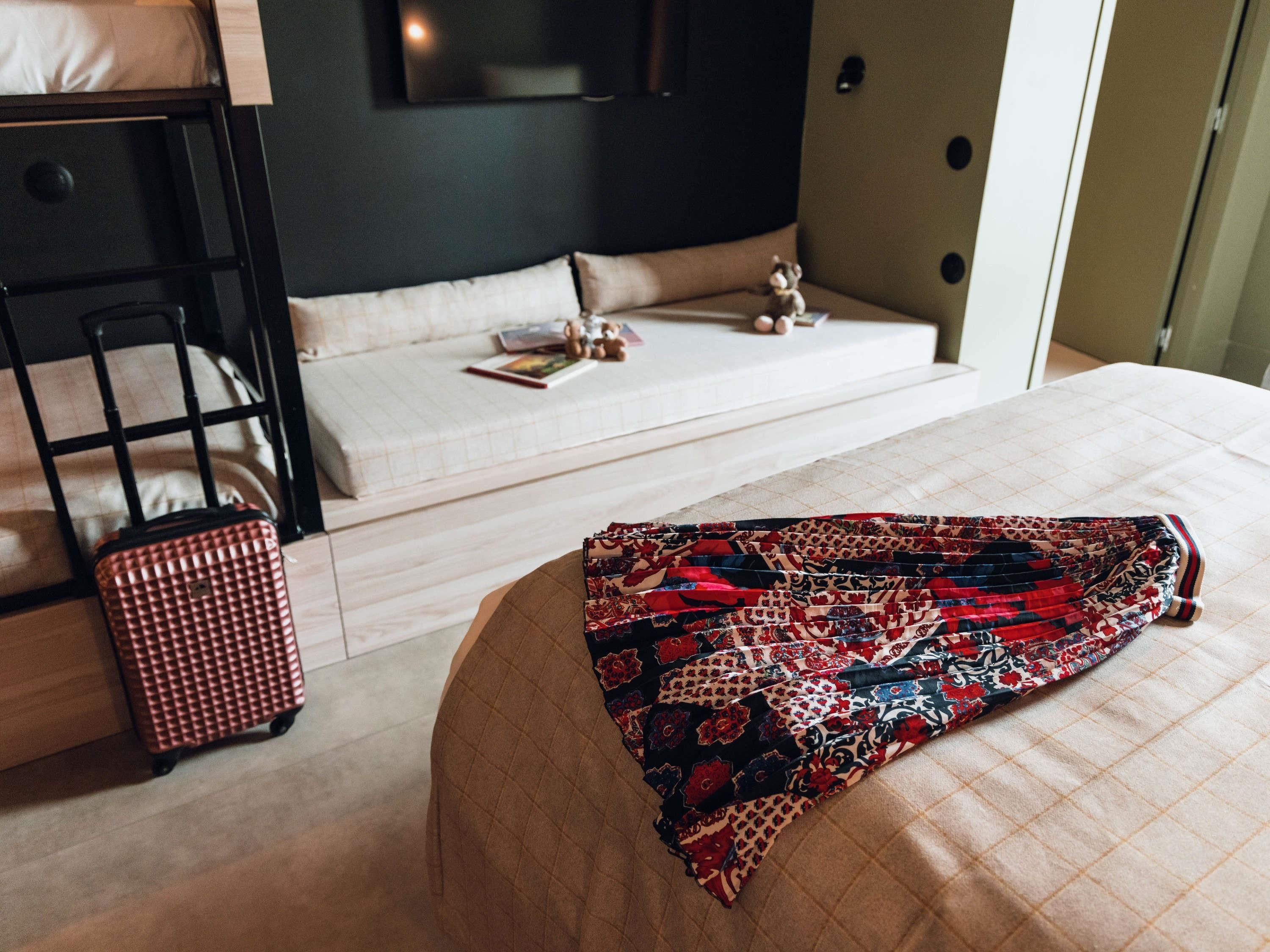Une chambre d’hôtel avec un lit, une valise, un canapé et un téléviseur.