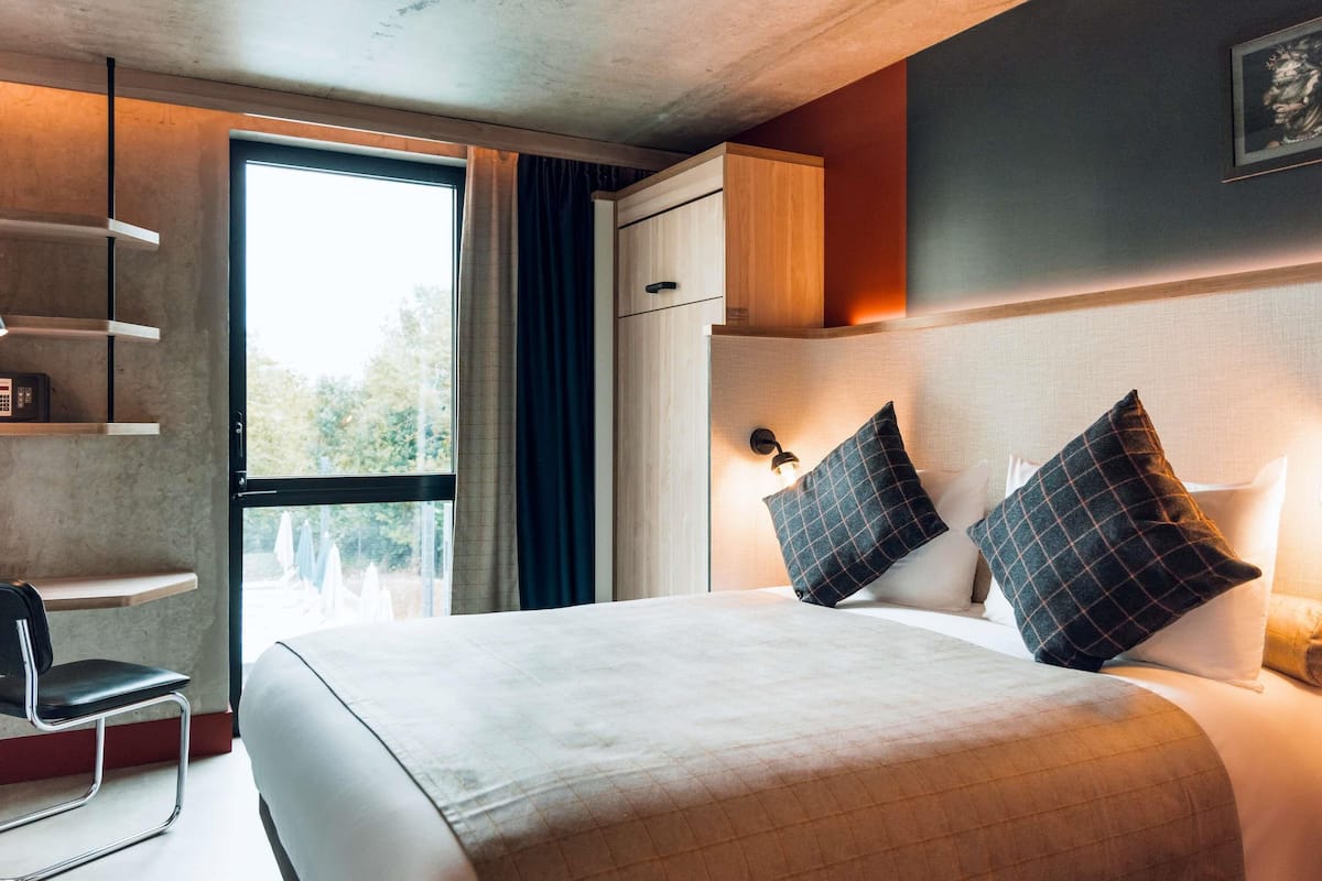 A modern hotel room with a large bed, a desk, and a chair.