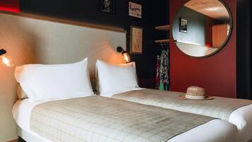A hotel room with two beds, a round mirror, and a wall-mounted light fixture.
