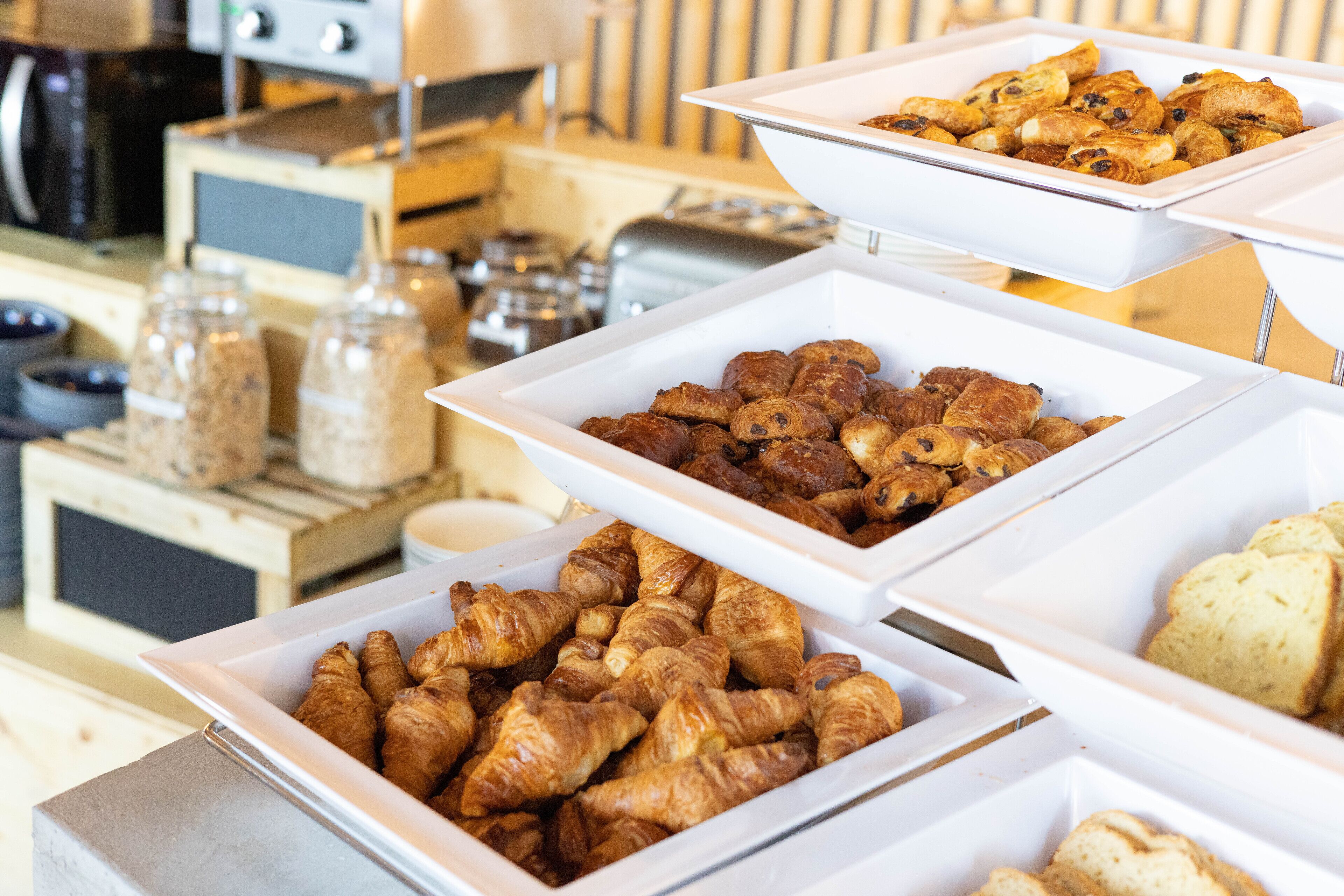A buffet with various baked goods, including croissants and pastries, arranged on tiered serving trays.