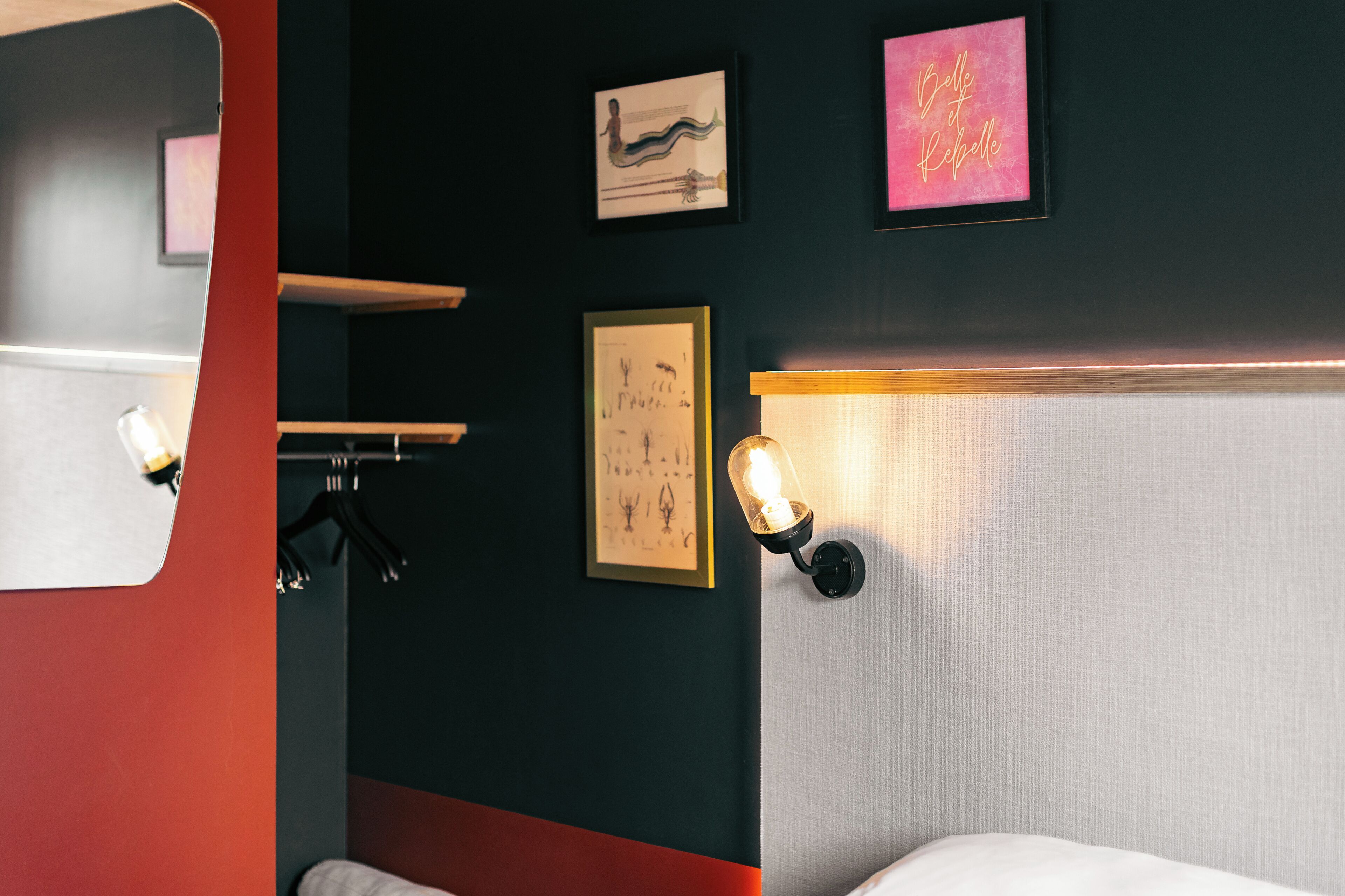 A hotel room with a bed, a mirror, and wall-mounted artwork.