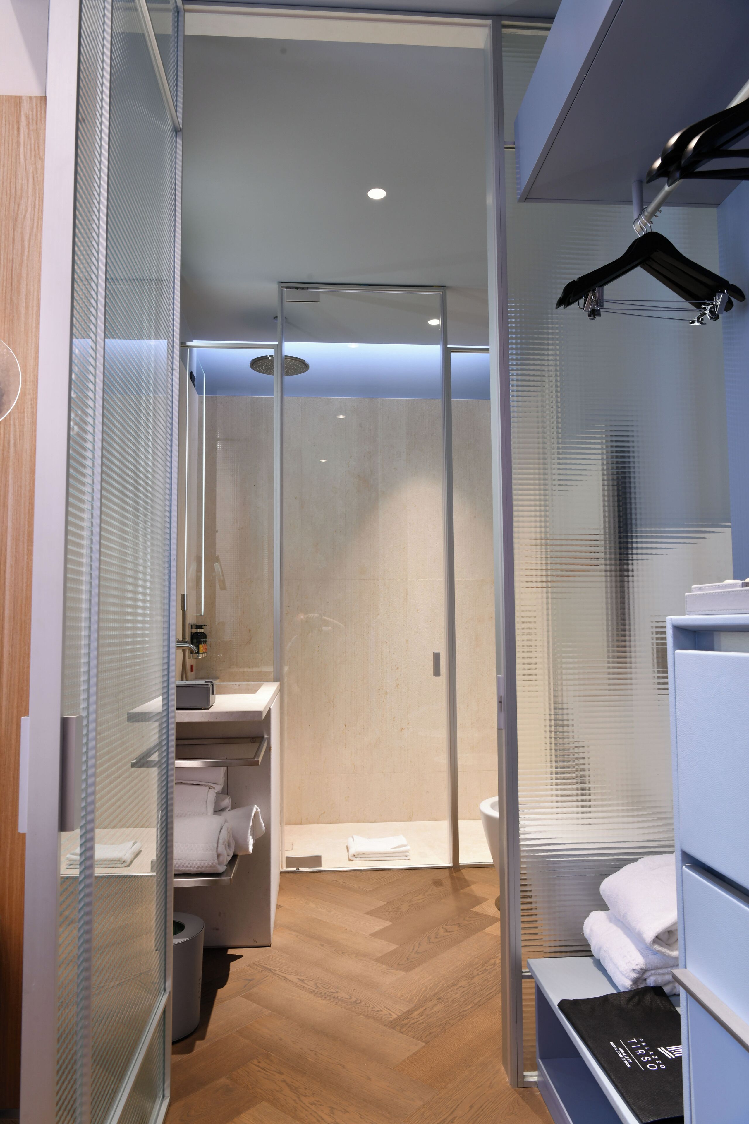 Un bagno moderno con box doccia in vetro, pavimento in legno e portasci asciugamani.