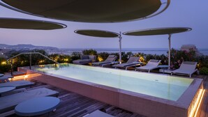 An infinity pool with lounge chairs and umbrellas, surrounded by wooden decking and overlooking a cityscape. - Palazzo Tirso Cagliari Mgallery (Cagliari)