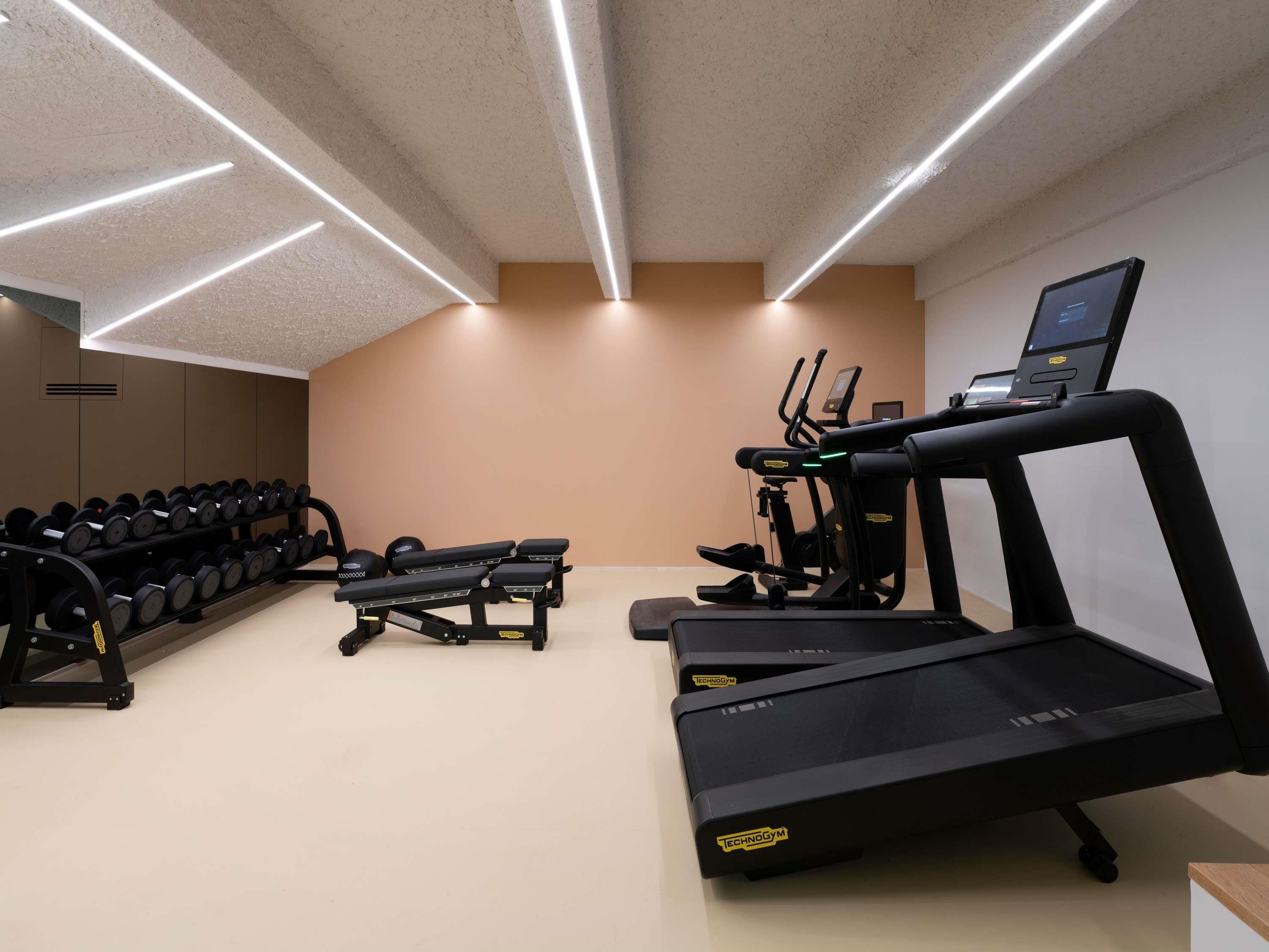 Un gimnasio con cintas de correr, elípticas y una prensa de banca.