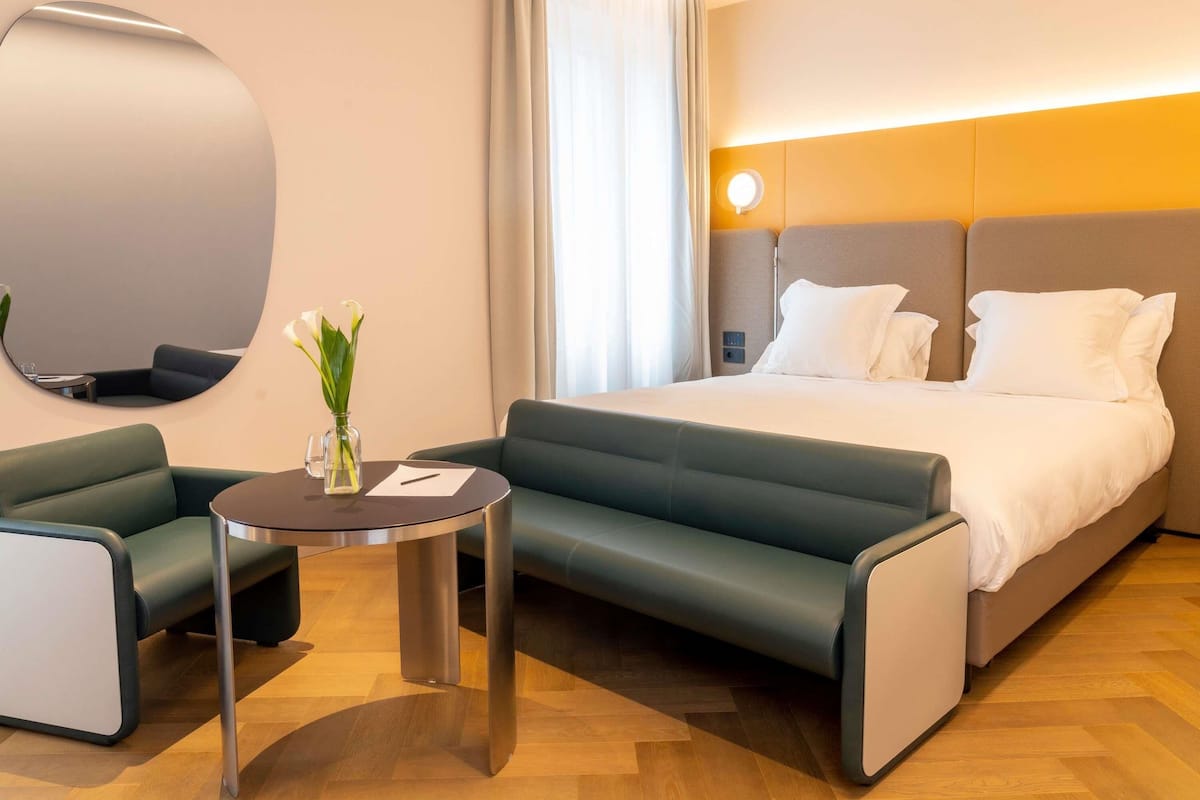 A modern hotel room with a bed, a sofa, a small table, and a mirror.