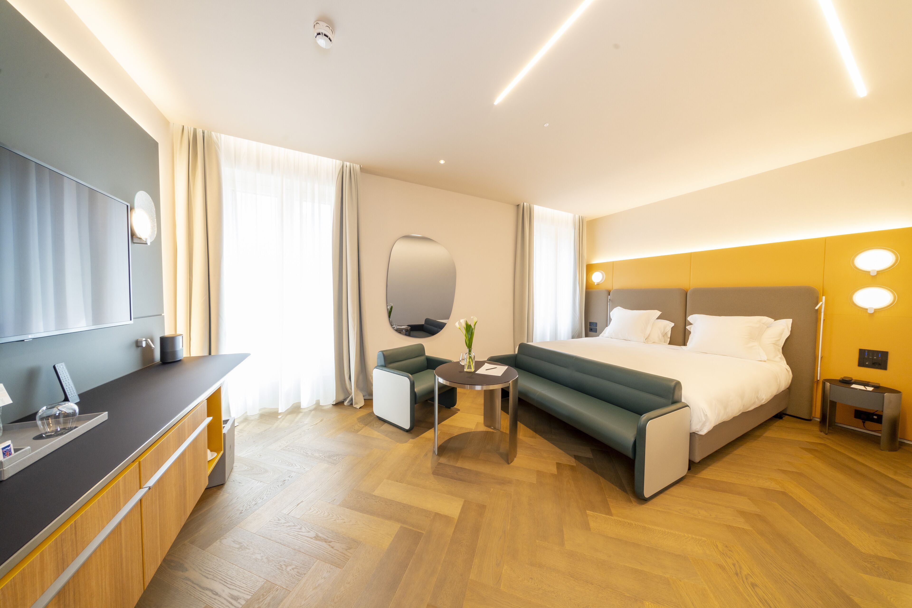 A modern hotel room with a bed, a desk, a chair, and a small table.