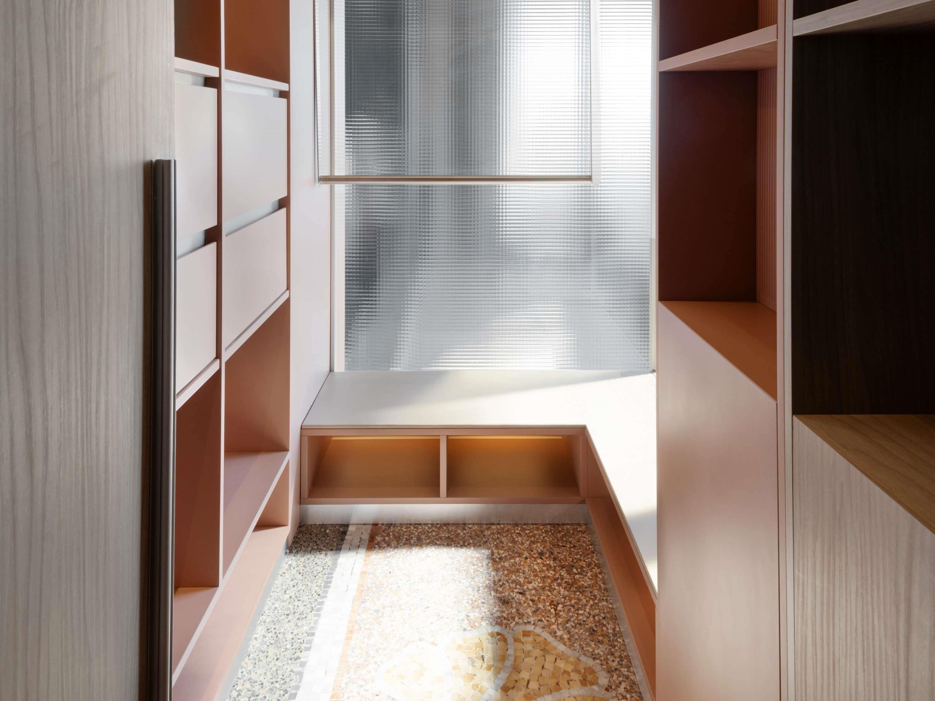 A modern closet with built-in shelves and a bench, a patterned rug, and a window with blinds.
