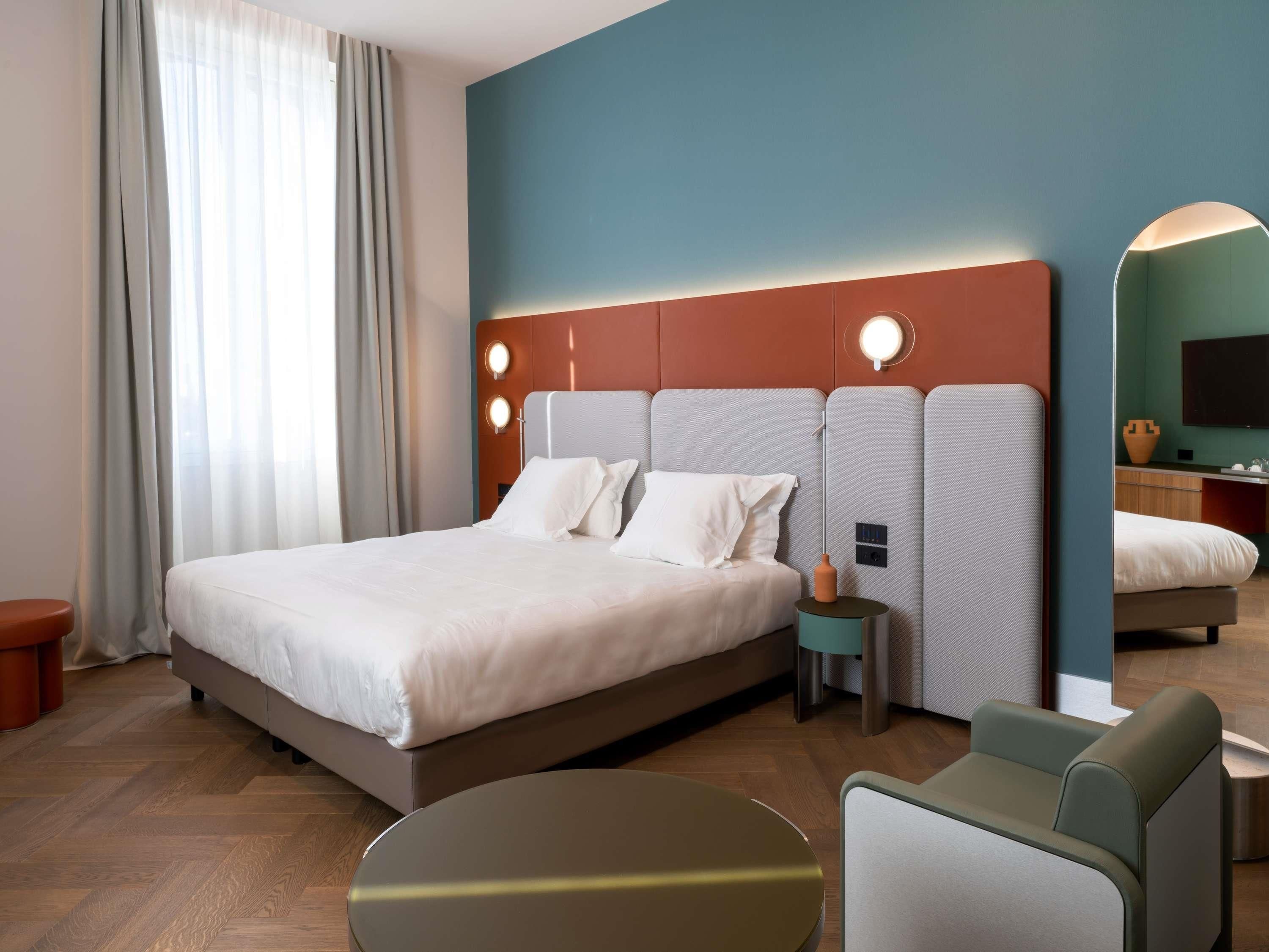 A modern hotel room with a large bed, a bedside table, a chair, and a small table.