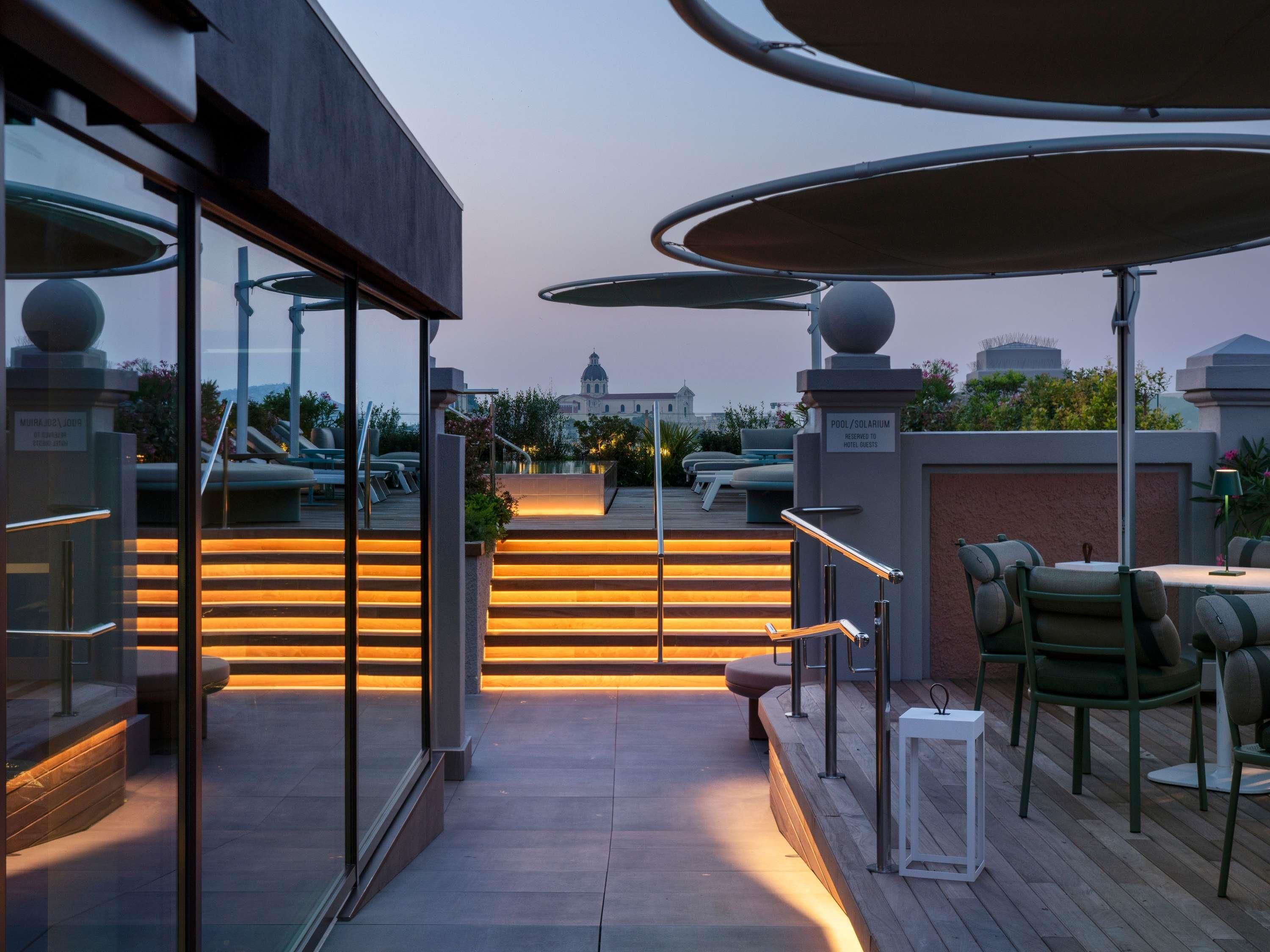 Eine Dachterrasse mit Sitzgelegenheiten im Freien, einem Pool und Blick auf ein historisches Gebäude im Hintergrund.