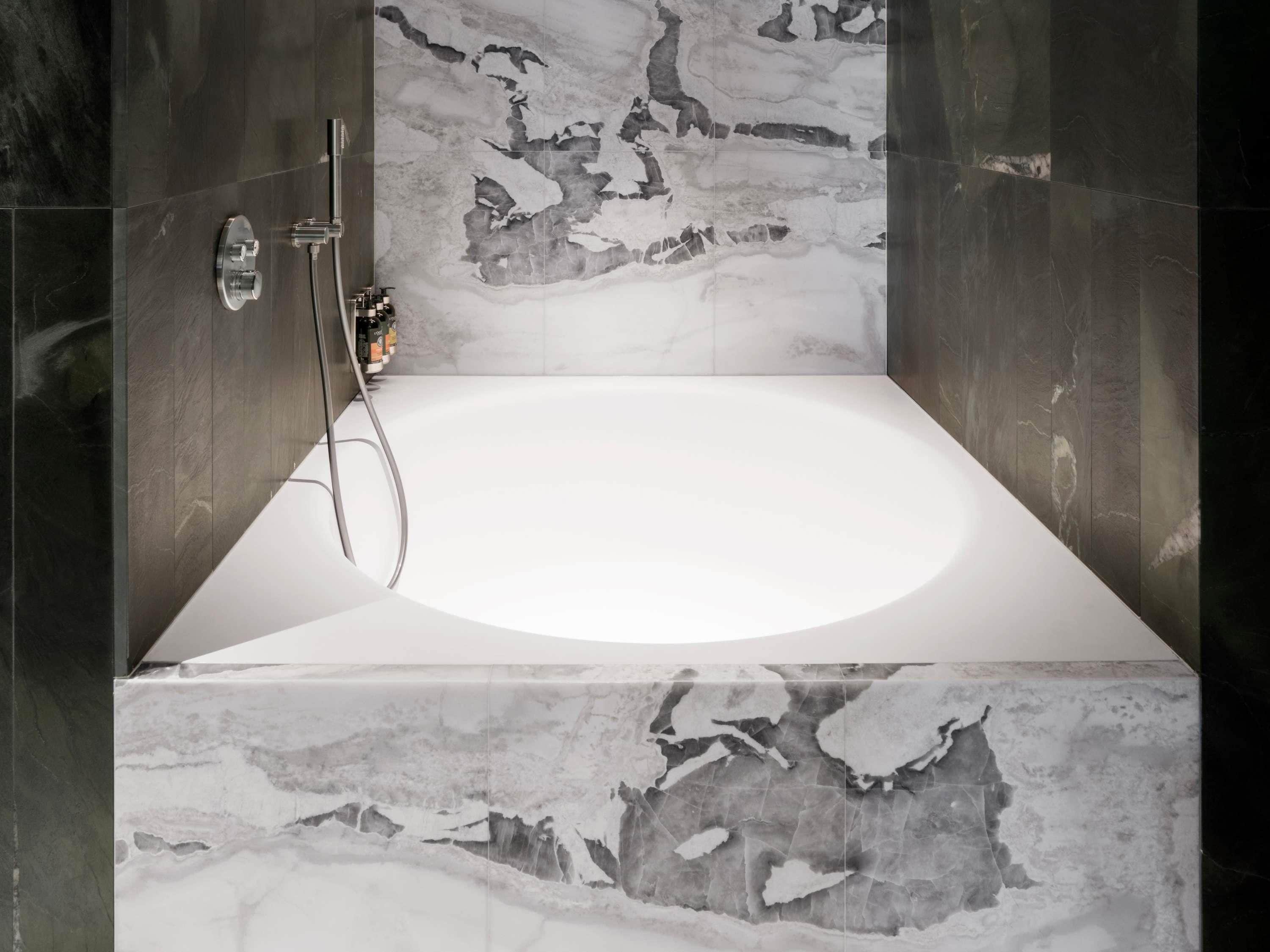 A modern bathroom with a marble sink, a handheld showerhead, and a large bathtub.