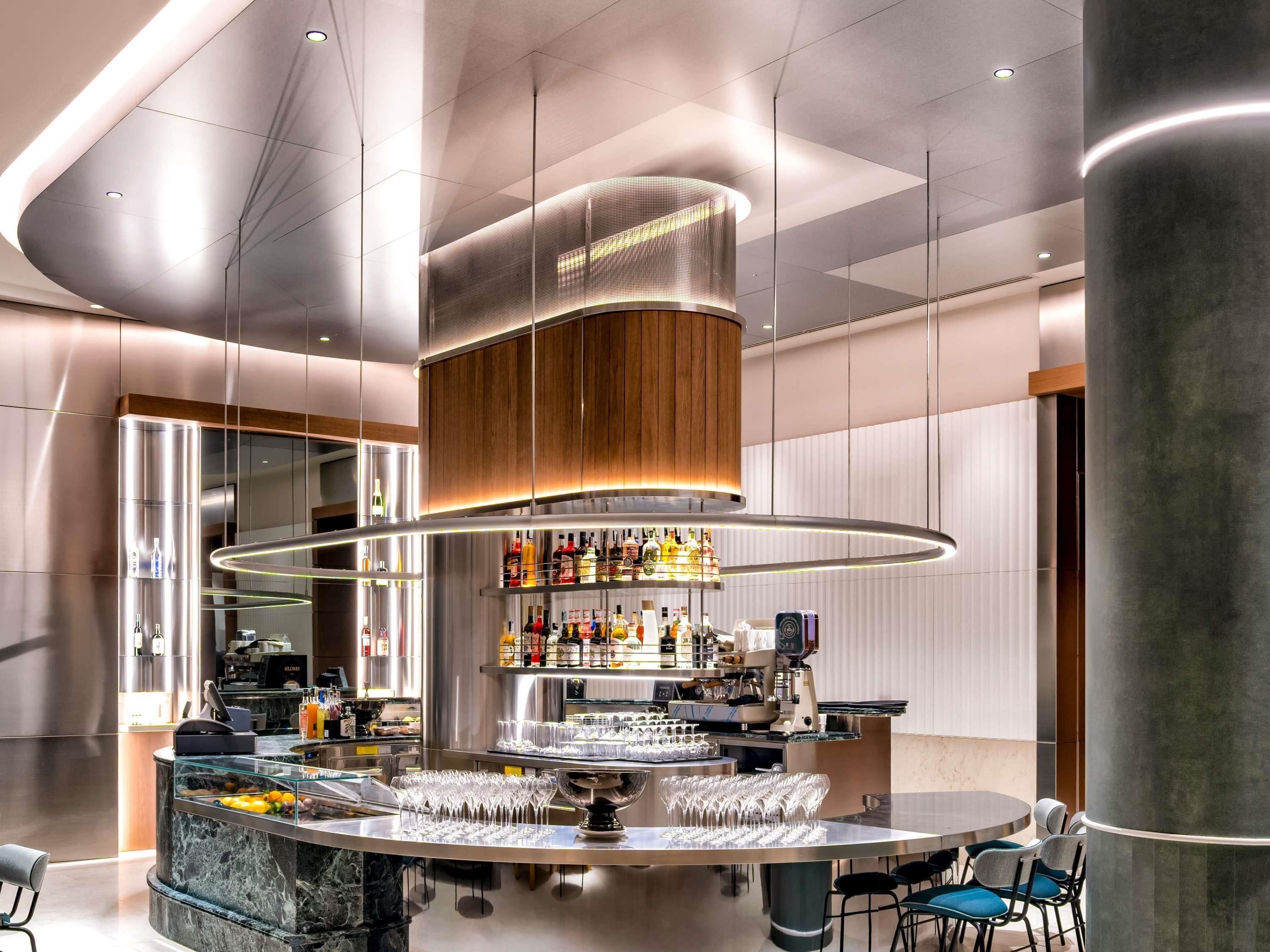 A modern bar area with a central circular bar, a variety of bottles, and a seating arrangement with chairs.