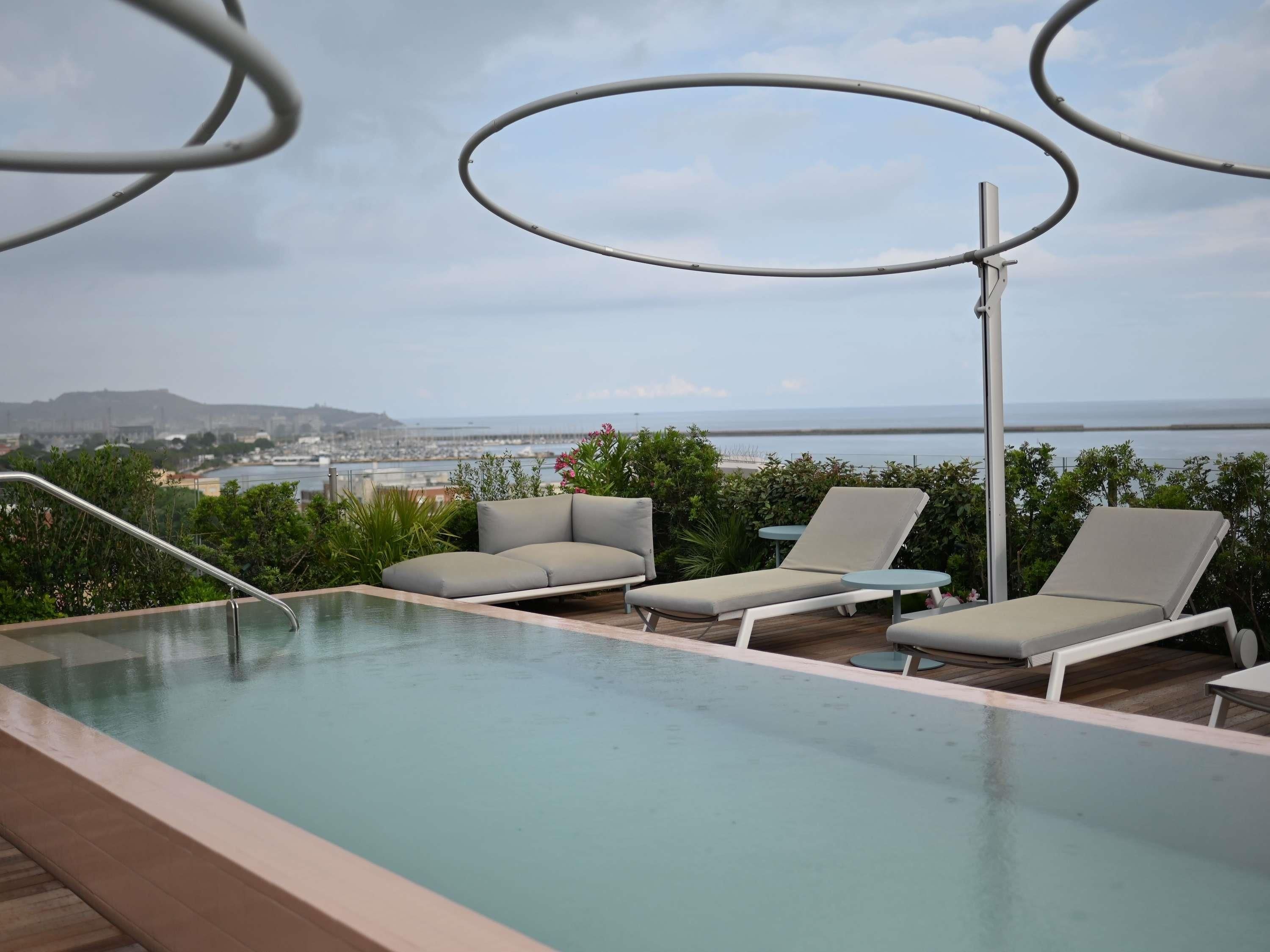 Une piscine extérieure à débordement, dotée de chaises longues et offrant une vue sur la mer.
