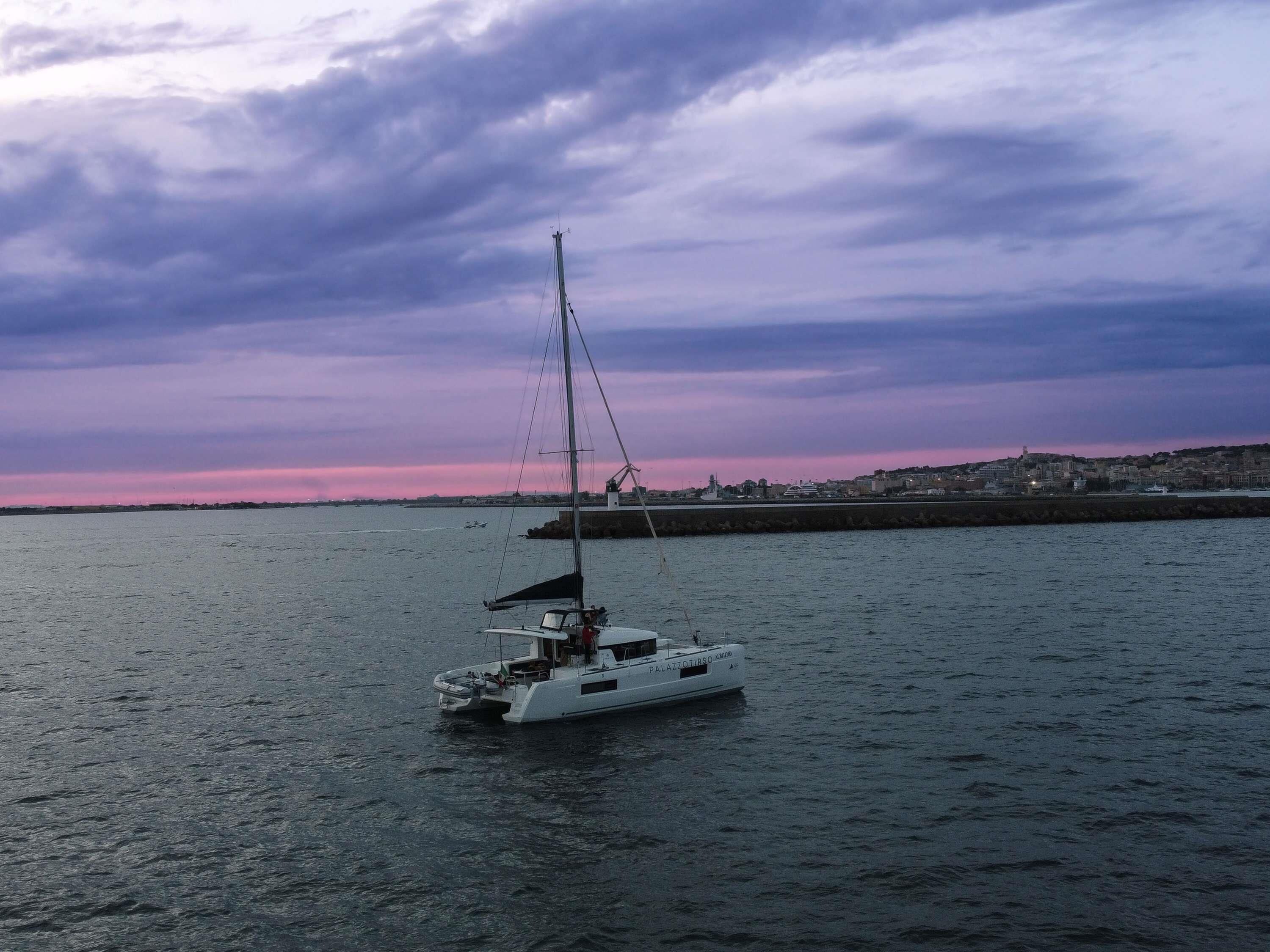 A sailboat on calm water with a cityscape in the background.