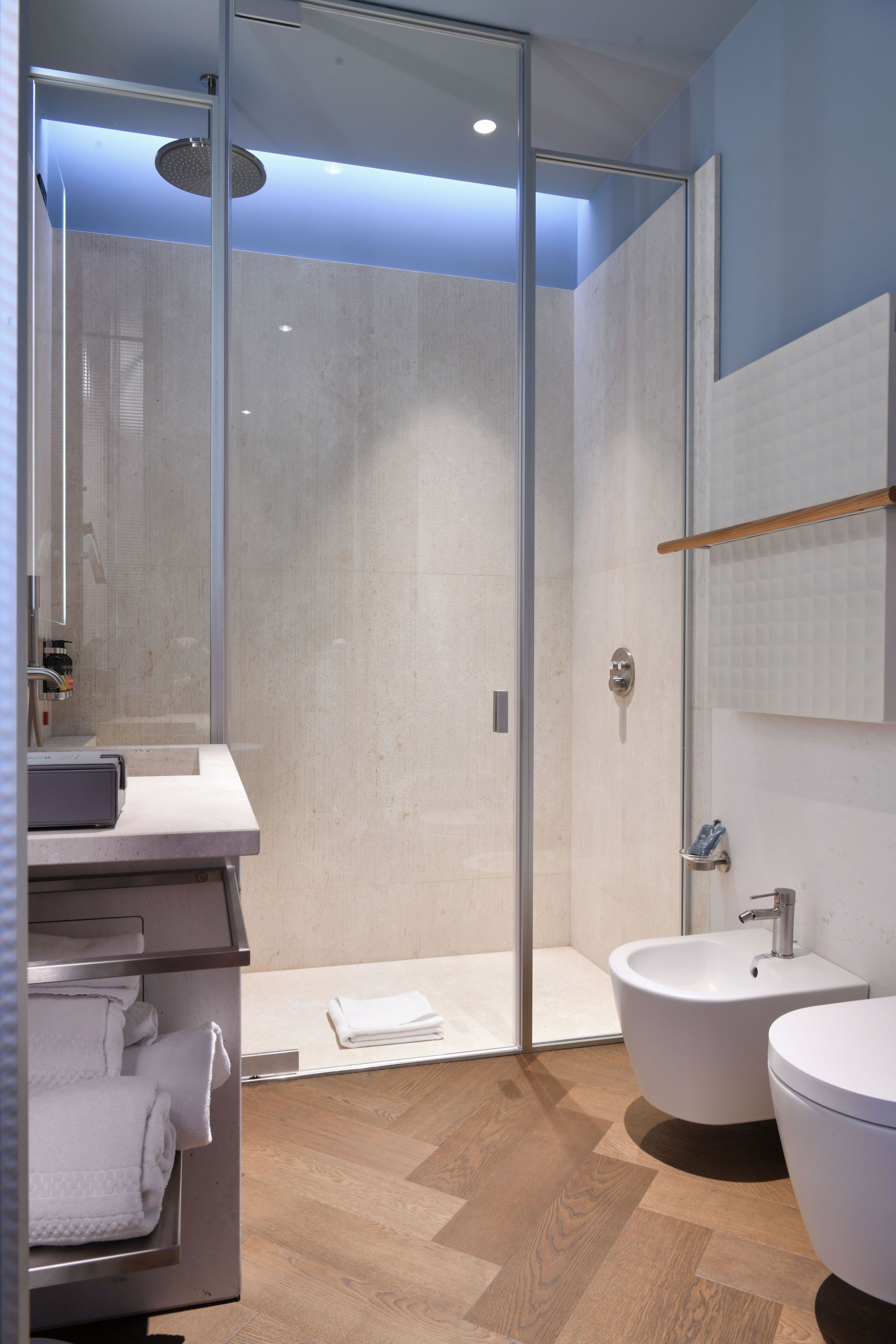 Un baño moderno con ducha acristalada, tocador con lavabo y un espejo grande.