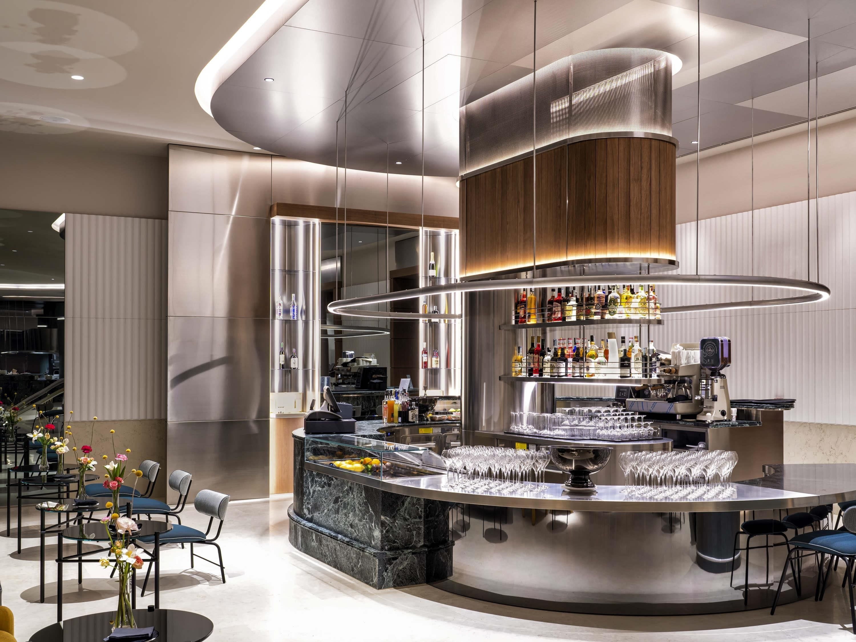 Un área de bar moderna con una barra curva, una máquina de café y una variedad de botellas y vasos.