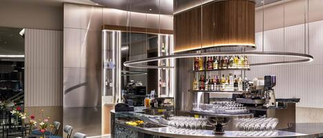 Un área de bar moderna con una barra curva, una máquina de café y una variedad de botellas y vasos.