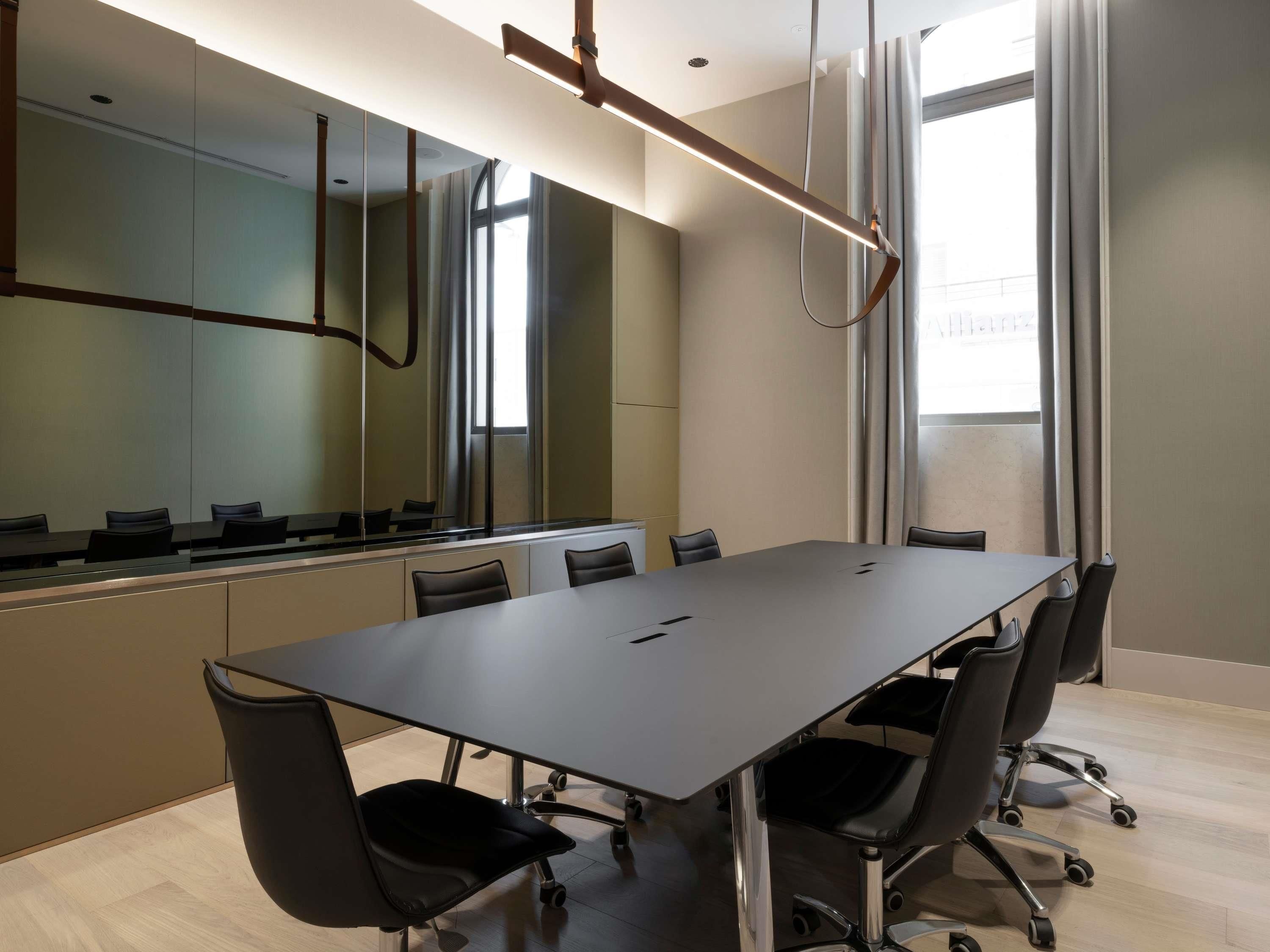 A conference room with a long table, black chairs, and a modern ceiling light fixture.