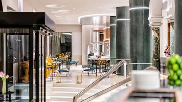 Un moderno vestíbulo de hotel con una escalera central, zonas de estar y un bar.