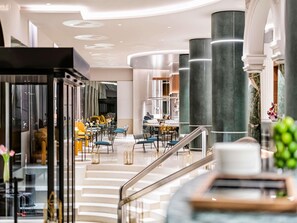 A modern hotel lobby with a central staircase, seating areas, and a bar. - Palazzo Tirso Cagliari Mgallery (Cagliari)