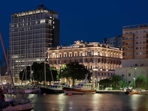 A waterfront hotel with a classic facade, a marina with boats, and modern high-rise buildings in the background. - Palazzo Tirso Cagliari Mgallery (Cagliari)