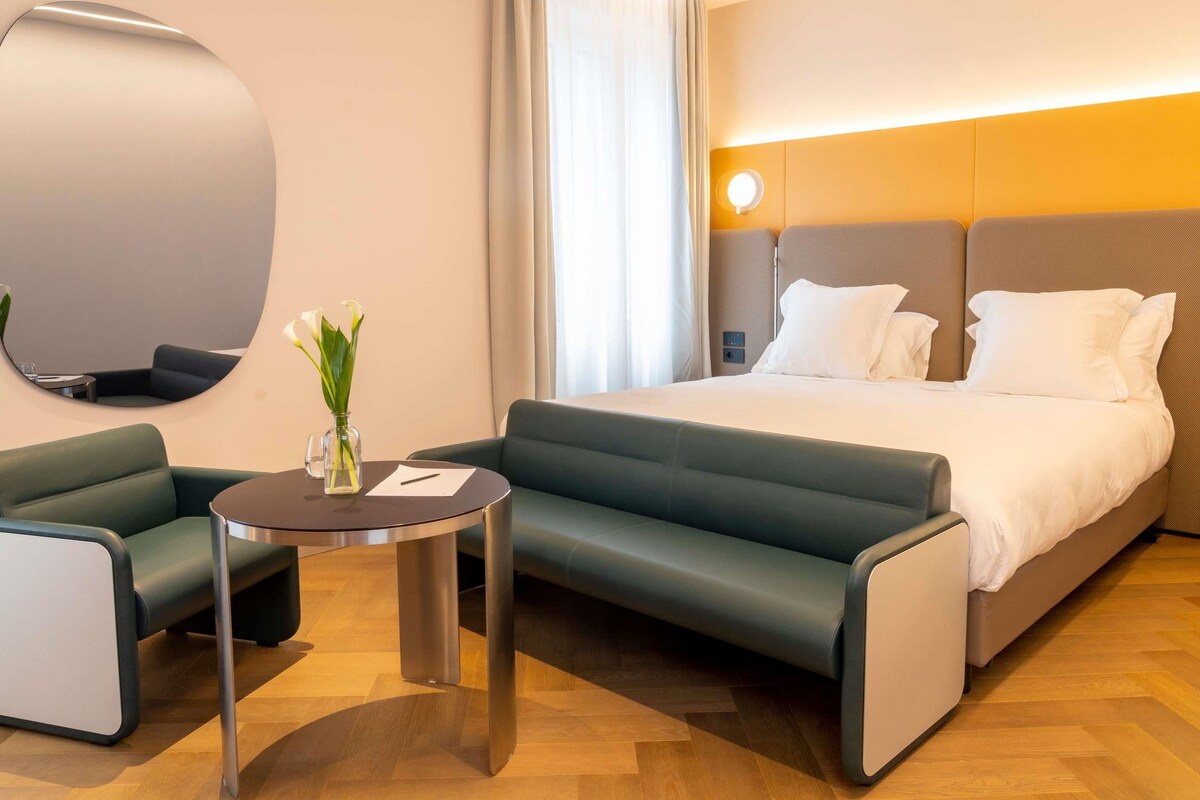 Une chambre d’hôtel moderne équipée d’un lit, d’un canapé, d’une petite table et d’un miroir.