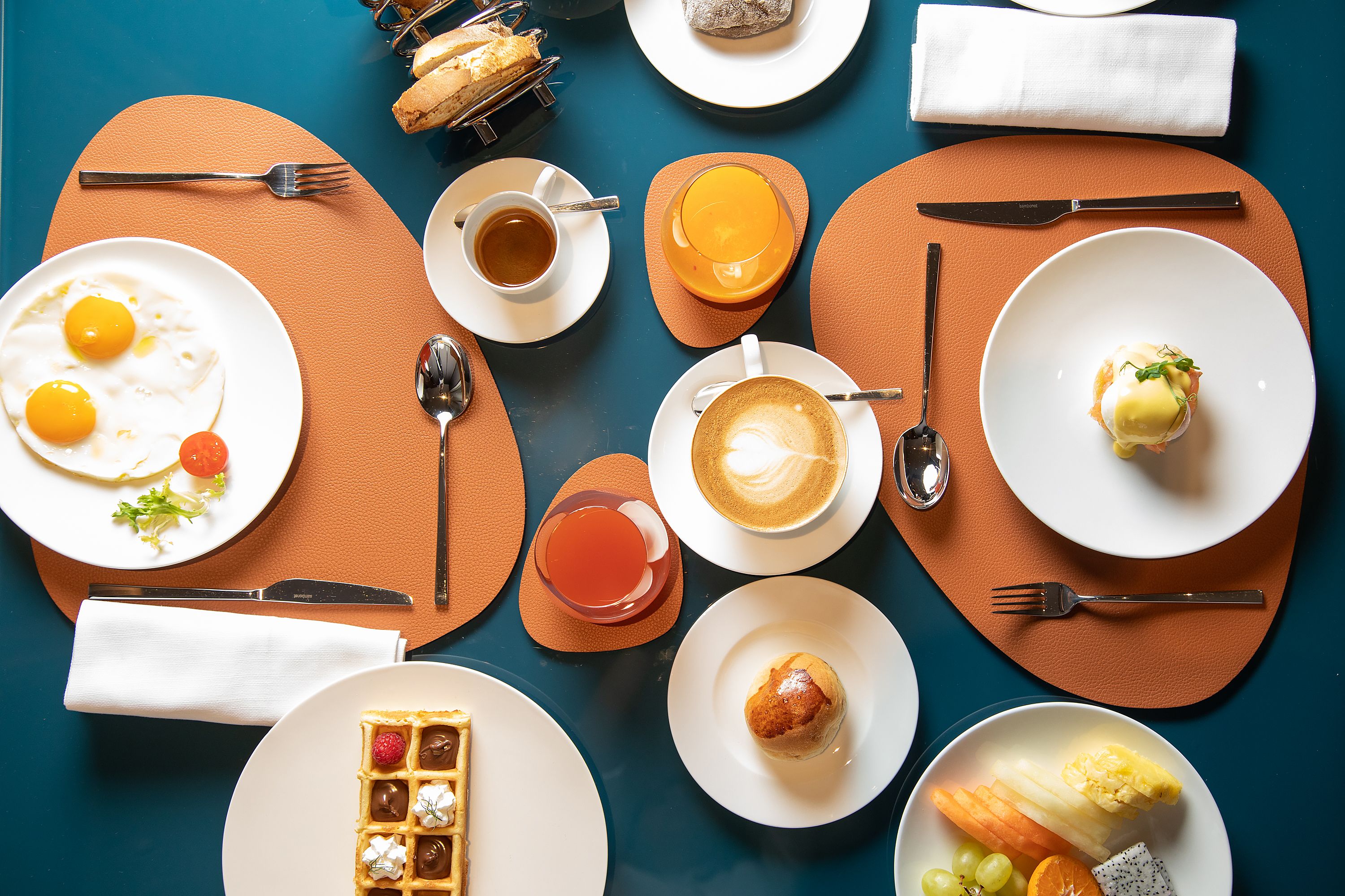 A breakfast setting with various dishes, including eggs, coffee, and pastries, arranged on a table with placemats.