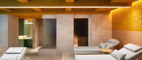 A spa room with three reclining chairs, a massage table, and a small table with a lamp.