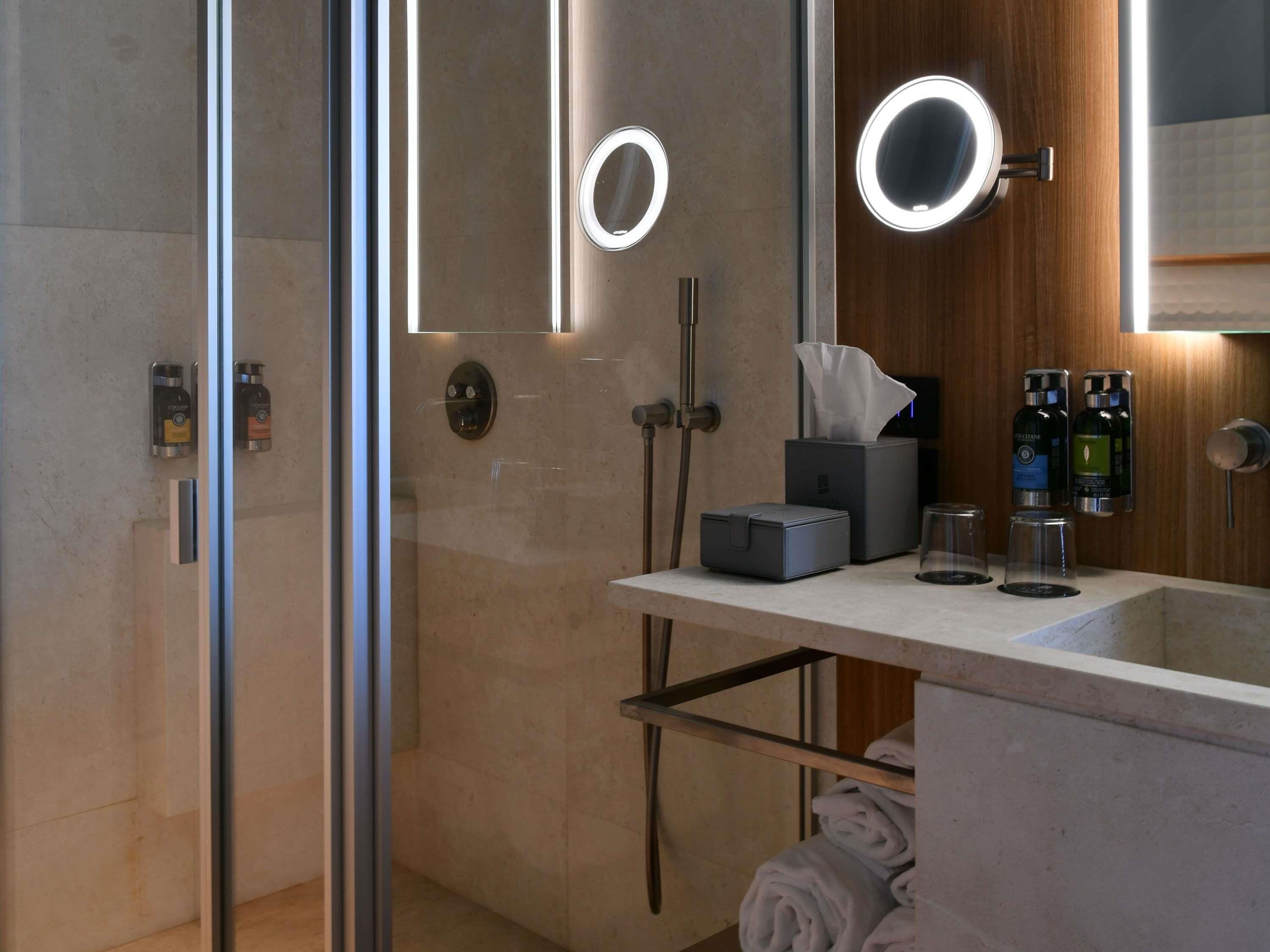 A modern bathroom with a glass shower enclosure, a vanity with a mirror, and toiletries.