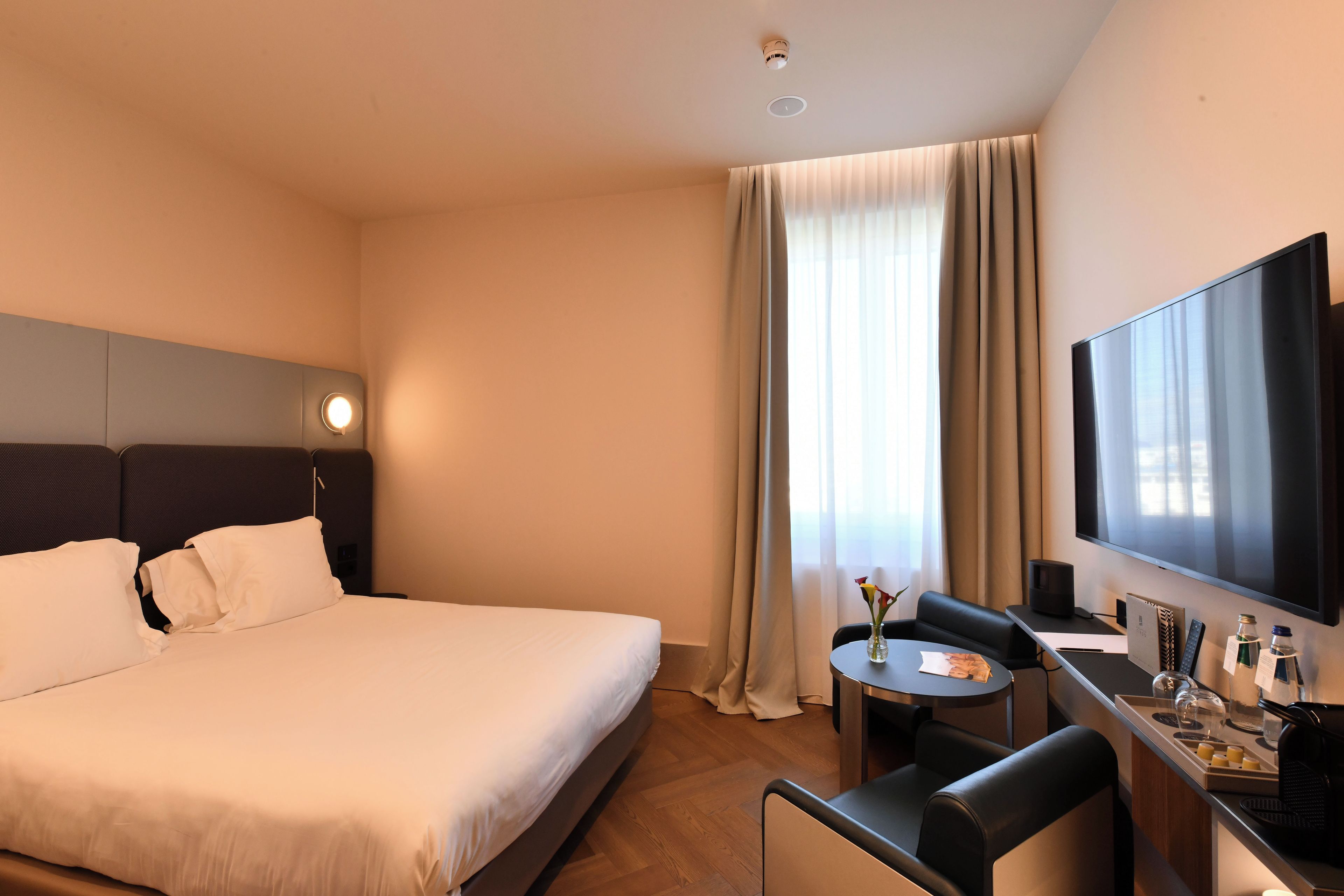 A hotel room with a bed, a desk with a chair, a television, and a window with curtains.