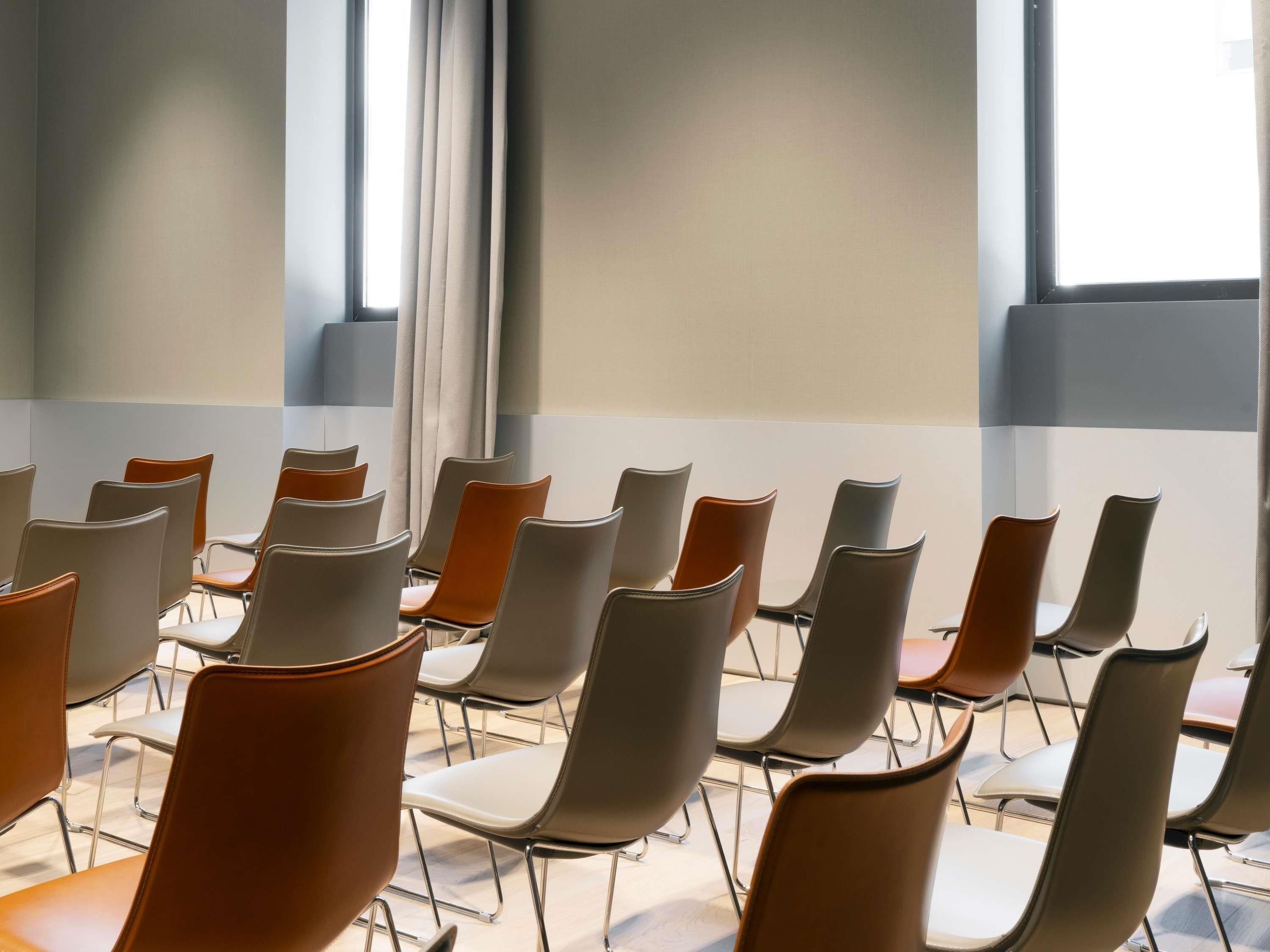 Un salón de conferencias con filas de sillas y un amplio ventanal con cortinas.