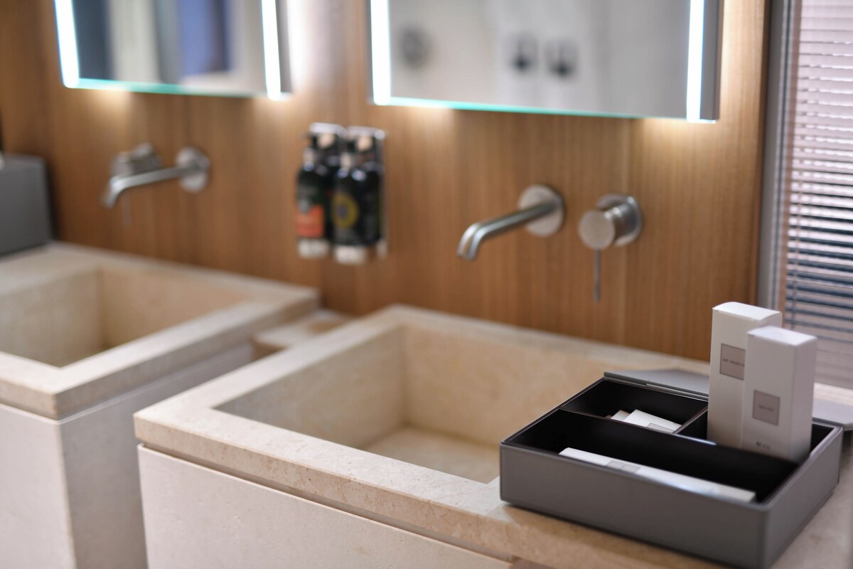 Een moderne badkamer met twee wasbakken, een spiegel en een zeepdispenser.