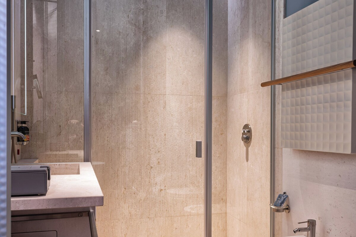 Een moderne badkamer met een glazen douchecabine, een houten vloer, een witte wastafel en een grote spiegel.
