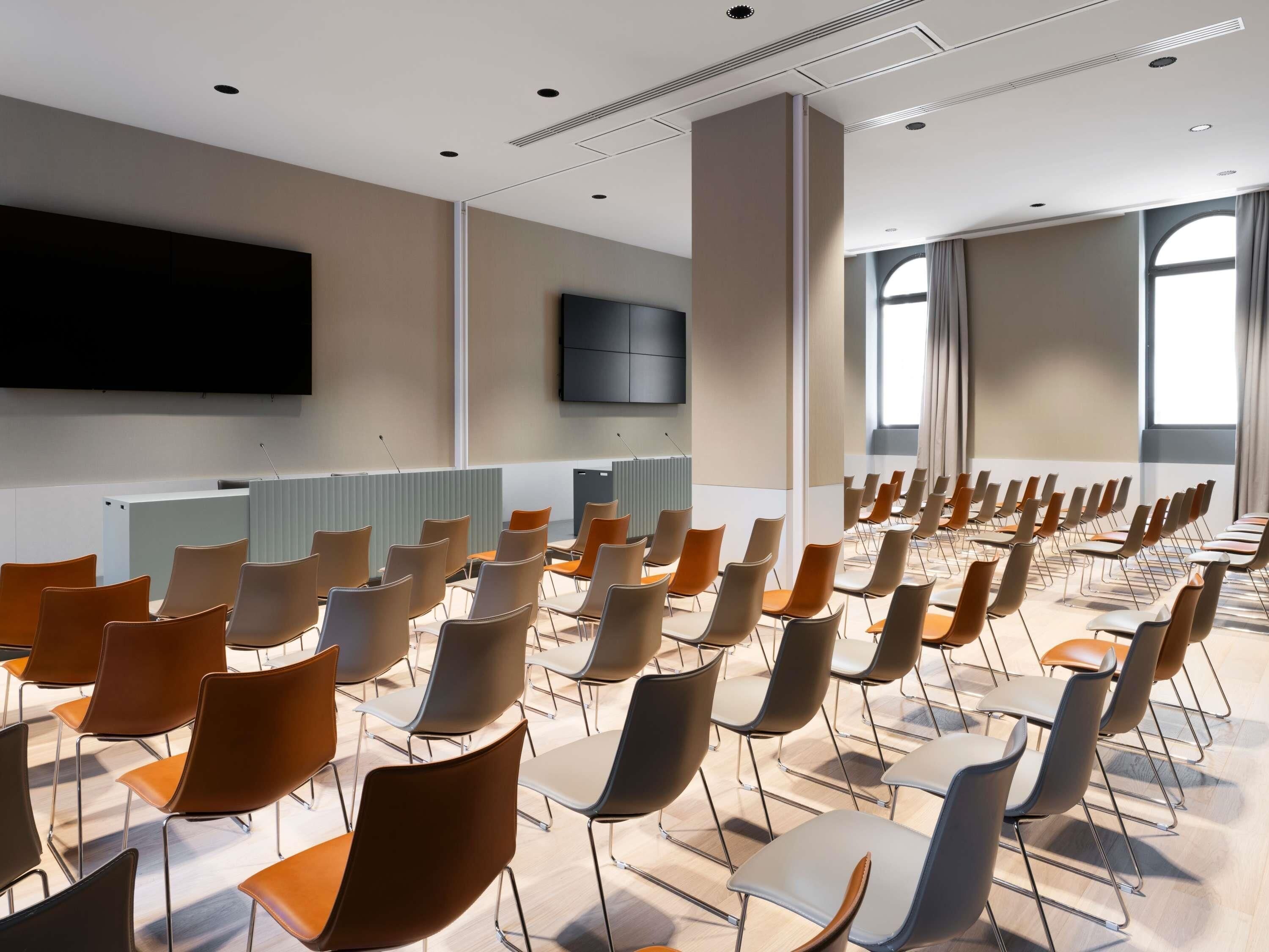 A conference room with rows of chairs, a flat-screen TV on the wall, and large windows.