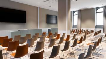 A conference room with rows of chairs, a flat-screen TV on the wall, and large windows.