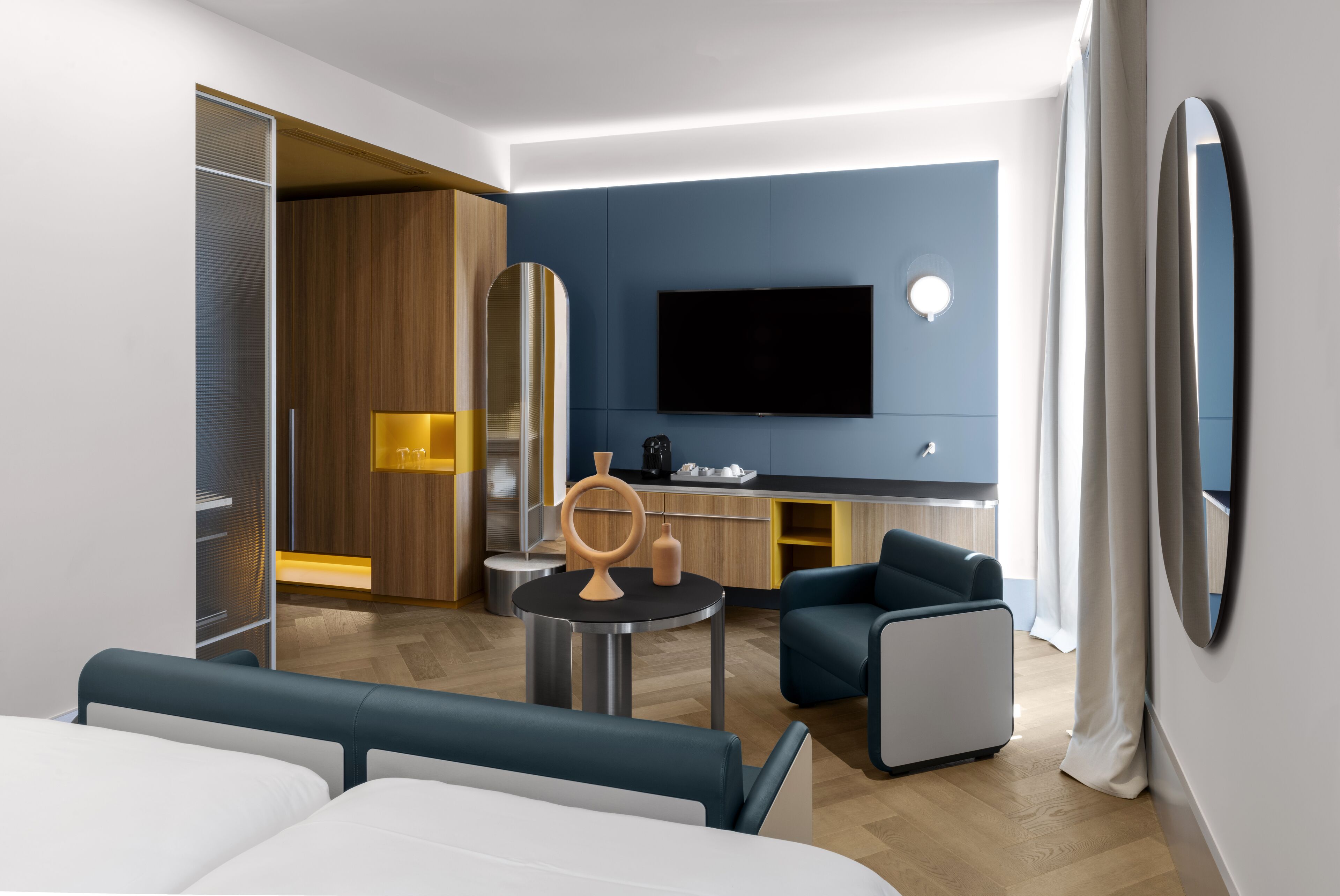 Une chambre d’hôtel moderne équipée d’un lit, d’un coin salon avec une table, d’une télévision et d’un minibar.