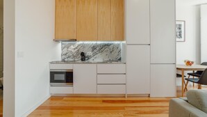 A compact kitchen with wooden cabinets, a marble countertop, a built-in oven, and a refrigerator. - Courtyard Oporto Design Apartment G (Porto)
