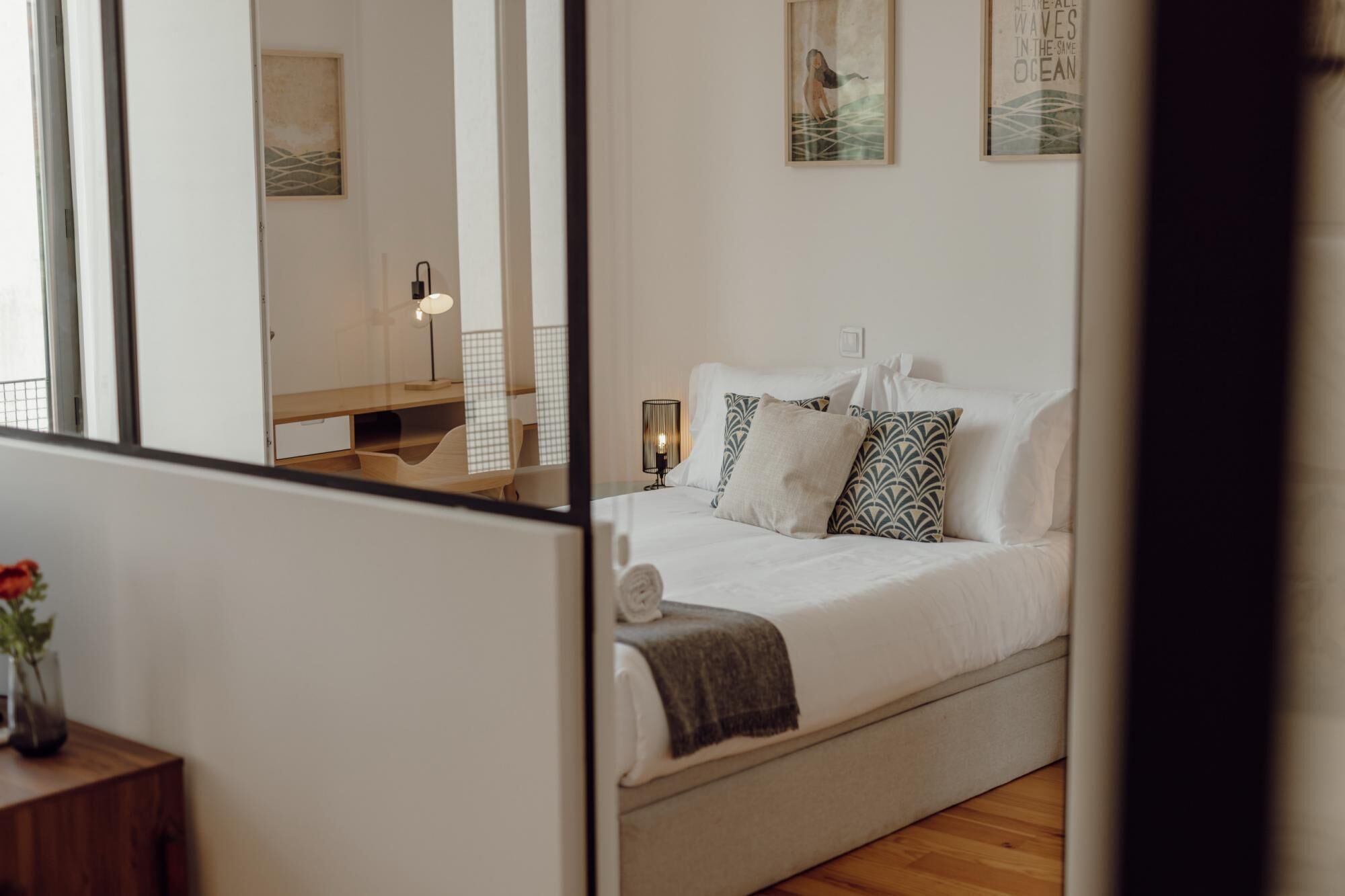 A bedroom with a bed, pillows, a bedside table, a lamp, and a wall with artwork.