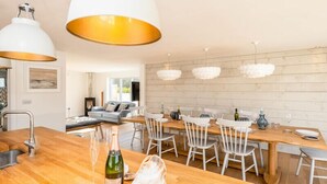 Une cuisine moderne avec un îlot central en bois, des suspensions blanches et un coin repas avec des chaises blanches et une table en bois.