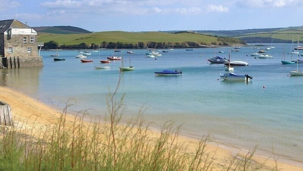 Un paysage côtier avec des bateaux sur une eau calme, une plage de sable et un bâtiment en pierre.