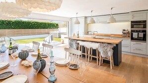 Une cuisine moderne avec un îlot central en bois, des luminaires suspendus et une vue sur un jardin verdoyant.