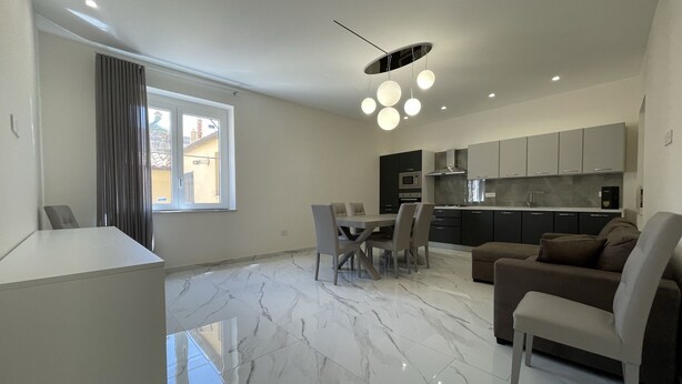 Une cuisine moderne avec des meubles de couleur sombre, un coin repas avec une table et des chaises, et un salon avec un canapé et une table basse.