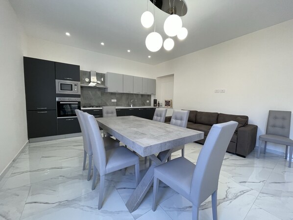 A modern kitchen with a dining area, featuring a marble floor, grey cabinetry, and a central island.