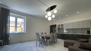 Une cuisine moderne avec des meubles de couleur sombre, un coin repas doté d’un sol en marbre et un canapé.