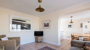 Ein Wohnzimmer mit Fernseher, Korbmöbeln, einem gemusterten Teppich und einem Essbereich mit Tisch und Stühlen.