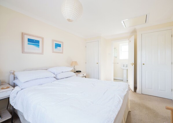 A bedroom with a large bed, a bedside table with a lamp, and a door leading to a bathroom. - Tresow (Wadebridge)