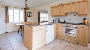 Una cocina con armarios de madera, una isla central, horno empotrado y una ventana con cortinas.