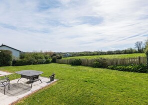 A well-maintained backyard with a patio table and chairs, a wooden fence, and a grassy lawn. - Tresow (Wadebridge)