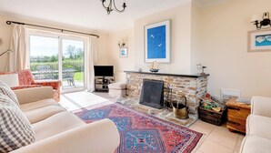 Ein Wohnzimmer mit Kamin, Fernseher, großem Fenster und einem gemusterten Teppich.